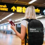 Rear view of a woman at the airport holding a passport with a boarding pass.