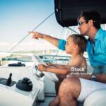 Father teaches his young son how to steer a yacht.