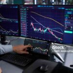 Busy Hispanic Stock Broker Using Multiple Monitors For Online Trading.