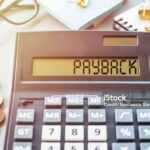 Word PAYBACK written on calculator on office table.