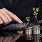 Midsection of businessman using calculator by stacked coins with plants on desk