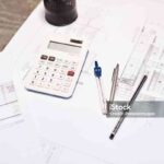 Shot of a calculator, pencil, blueprint and compass on a desk in an office